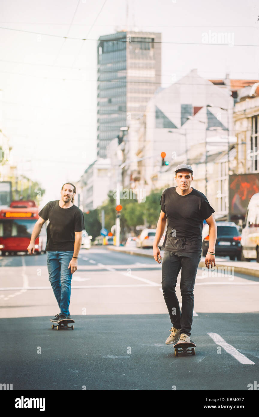 Due skateboard pro rider giro pattinare nella parte anteriore della vettura sulla città strada attraverso il traffico Foto Stock