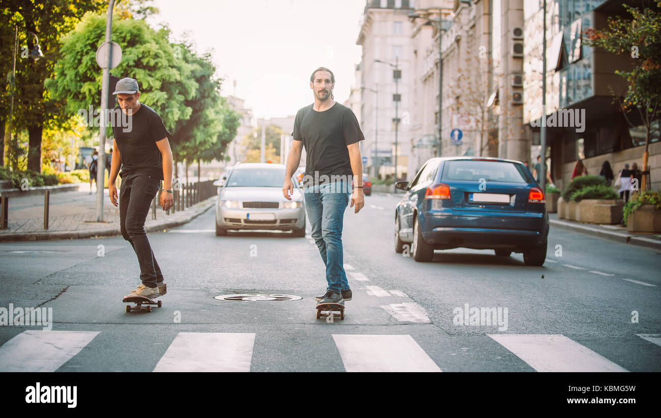 Due skateboard pro rider giro pattinare nella parte anteriore della vettura sulla città strada attraverso il traffico Foto Stock