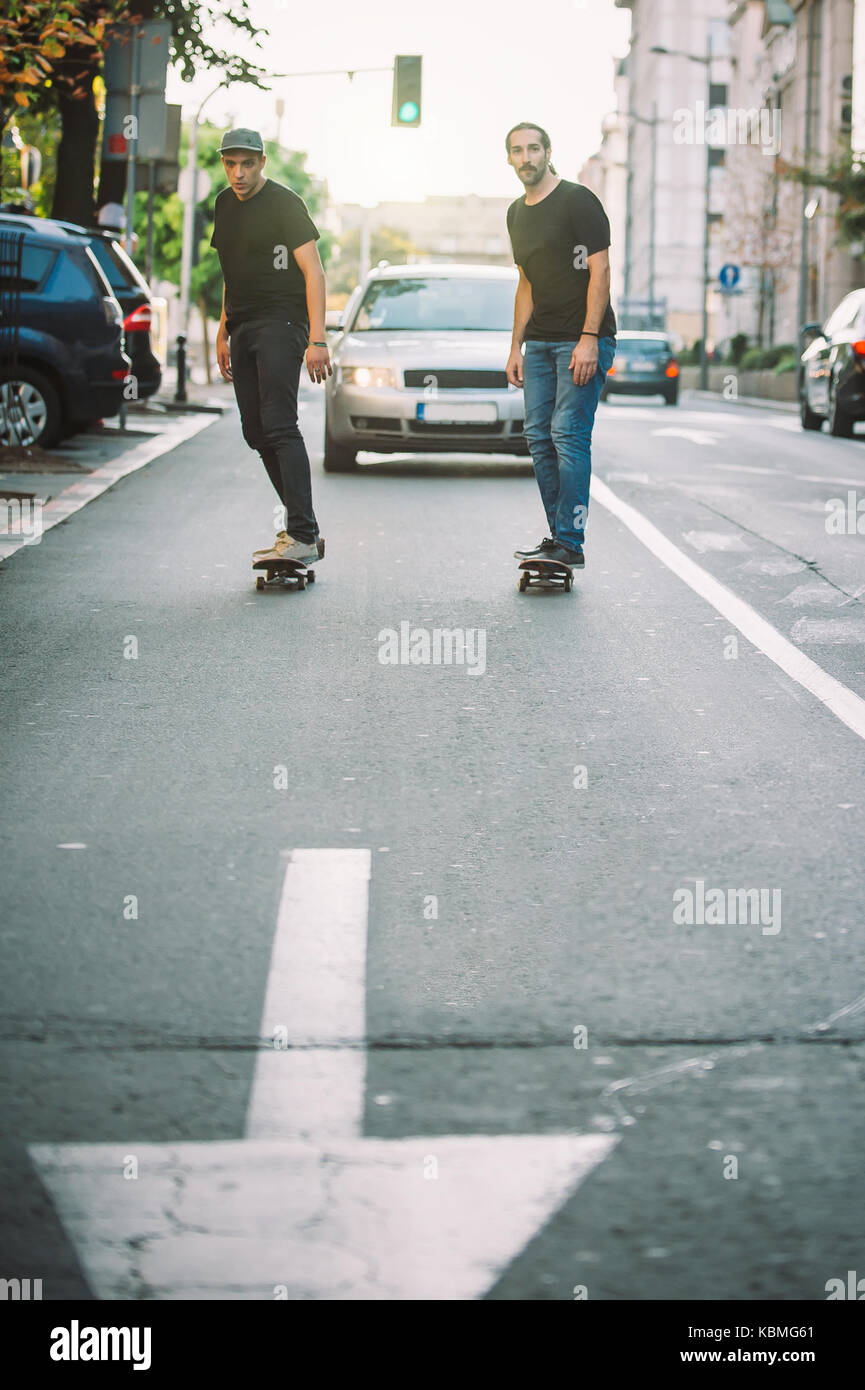 Due skateboard pro rider giro pattinare nella parte anteriore della vettura sulla città strada attraverso il traffico Foto Stock