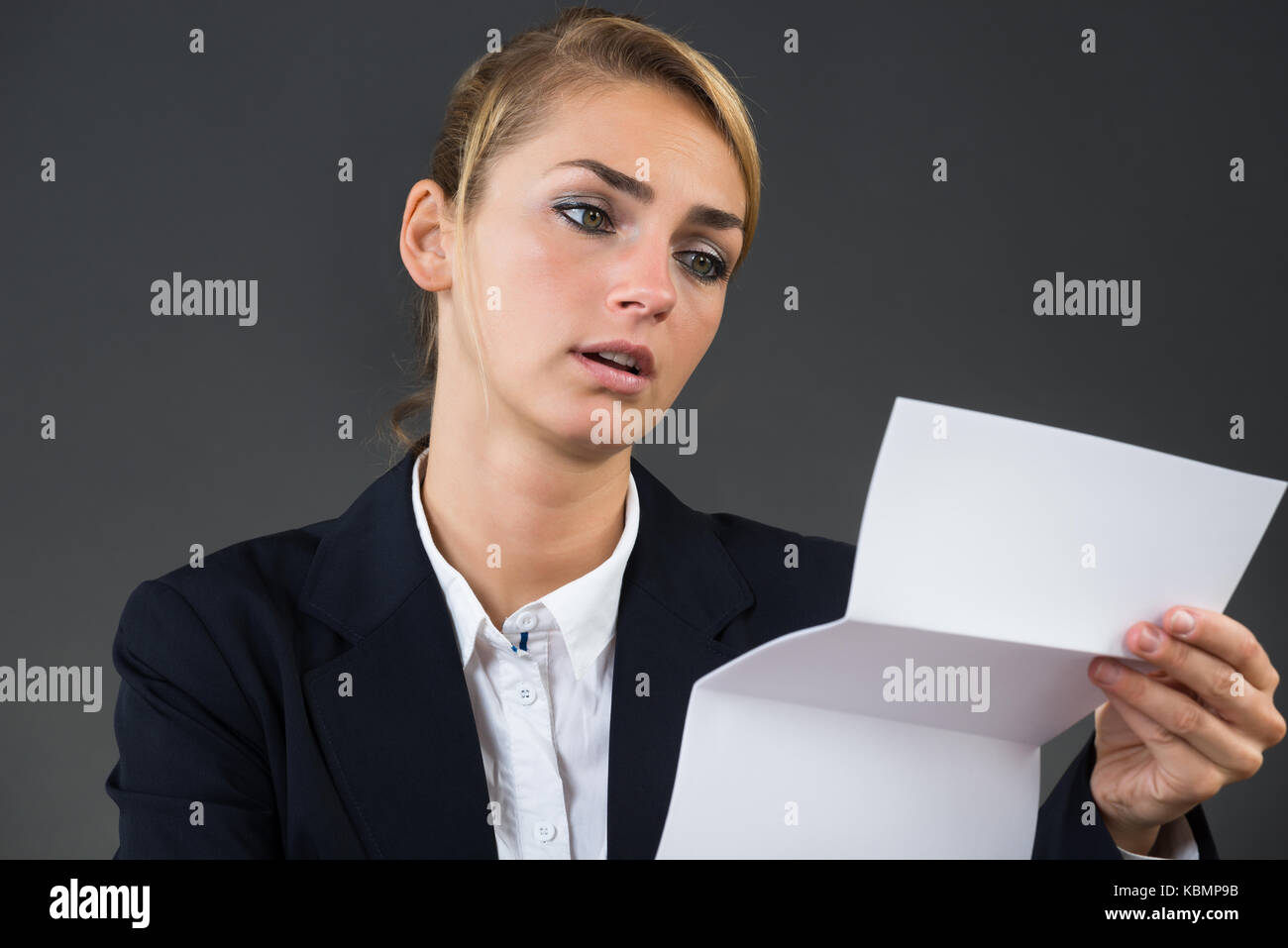 Scioccato giovane imprenditrice lettura la lettera al banco su sfondo grigio Foto Stock