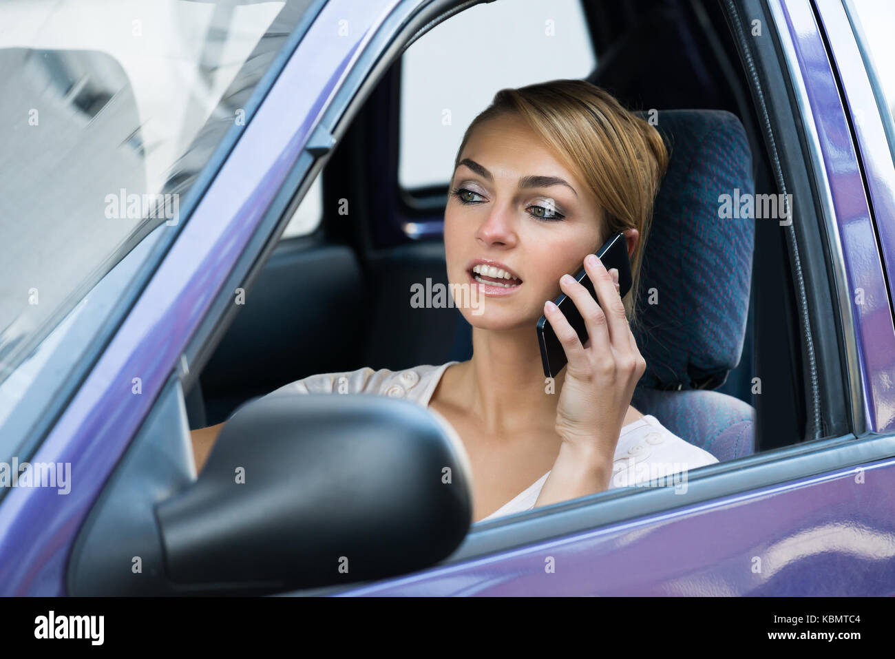Giovane donna utilizzando il telefono cellulare mentre si guida auto Foto Stock