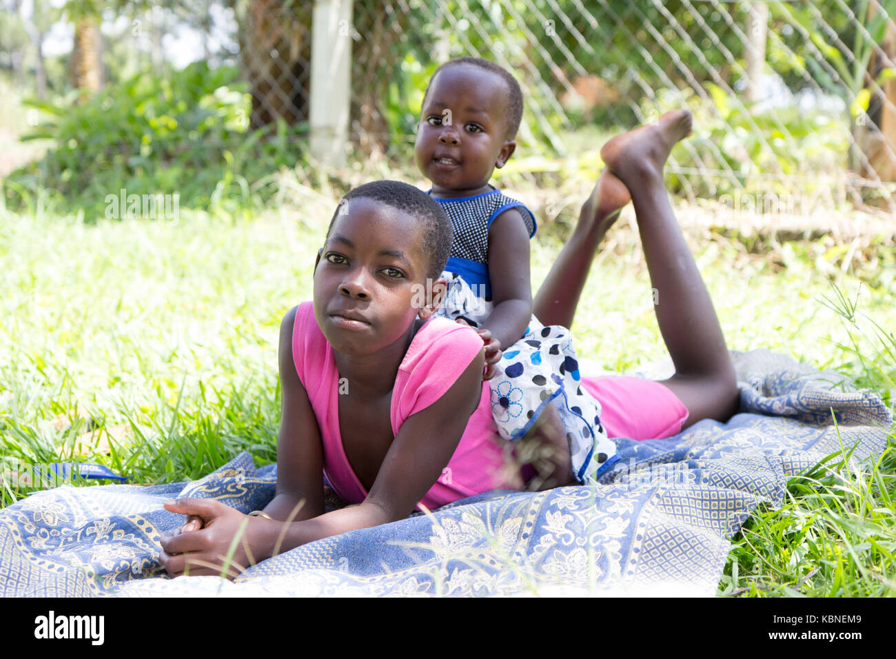 Makindu, Uganda. 27 aprile 2017. Due ragazze nere che giacciono nell'erba. Il piccolo è seduto sulla schiena delle ragazze più anziane. Foto Stock