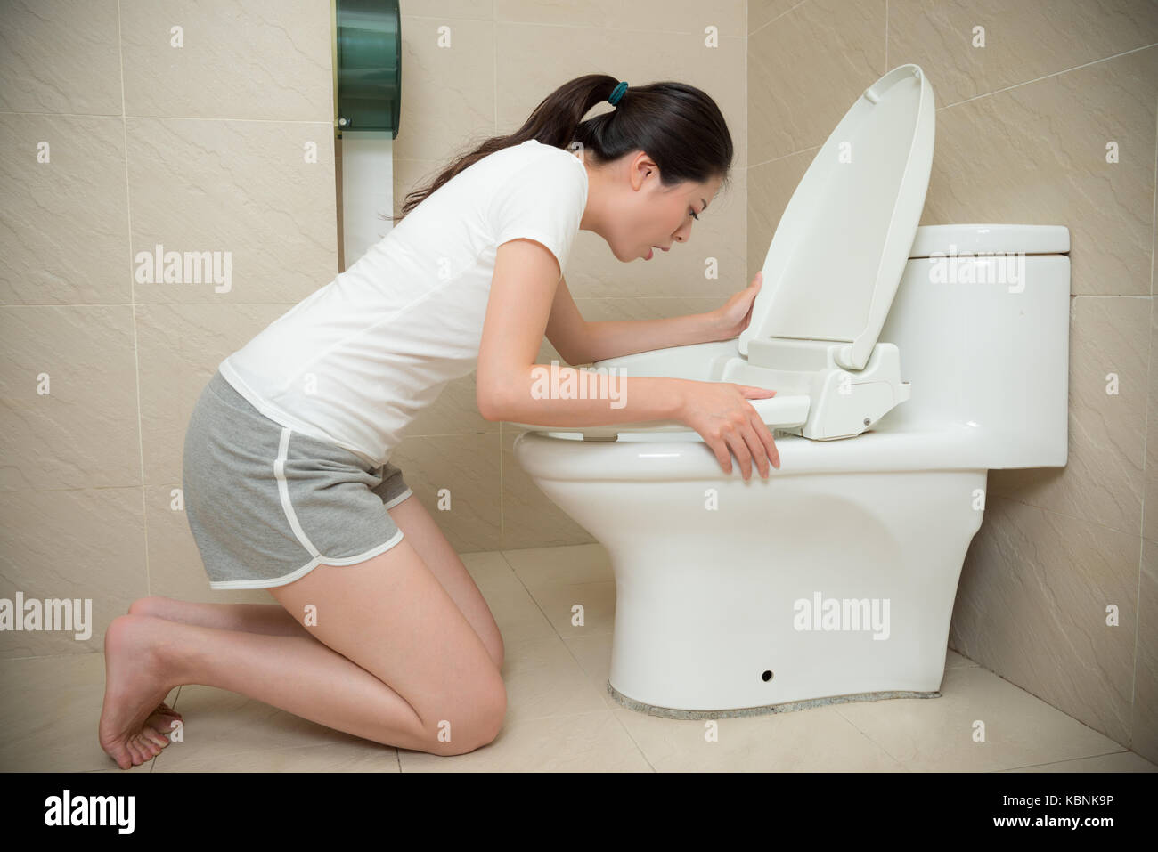 Bella ragazza dolce getting gravidanza sensazione di nausea e di solito in ginocchio di fronte a servizi igienici vomito in bagno a casa. Foto Stock
