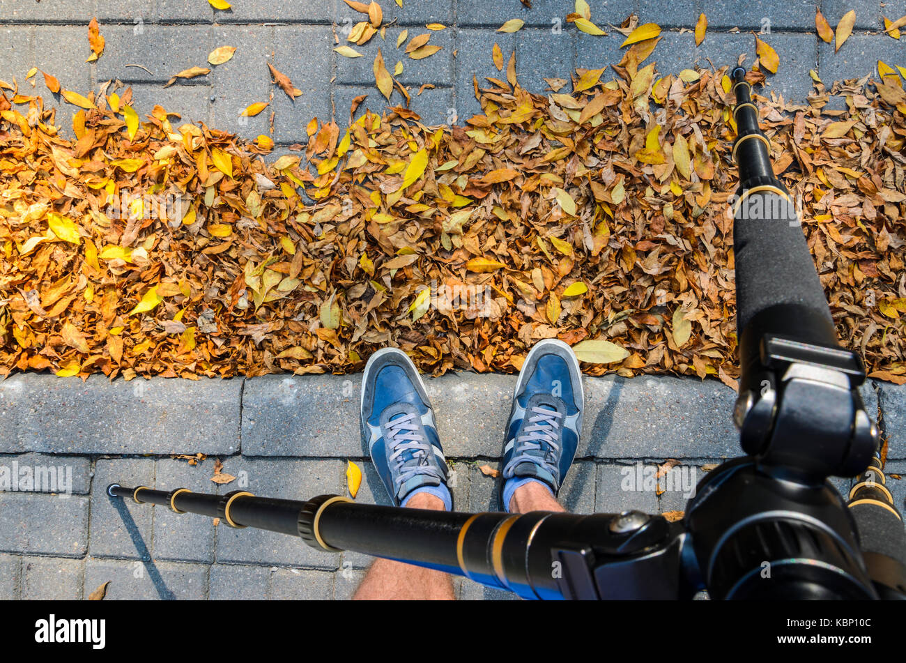 Vista da un treppiede ai piedi di un fotografo di fotografare la texture di pietre per pavimentazione in autunno. blu sneakers su una pavimentazione di colore grigio Foto Stock