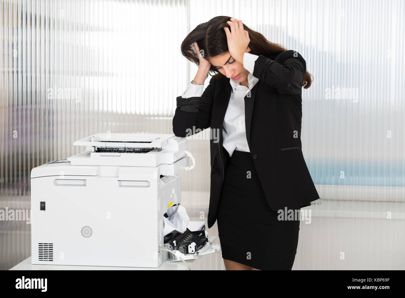 Irritato giovane imprenditrice guardando la carta bloccata nella stampante in ufficio Foto Stock