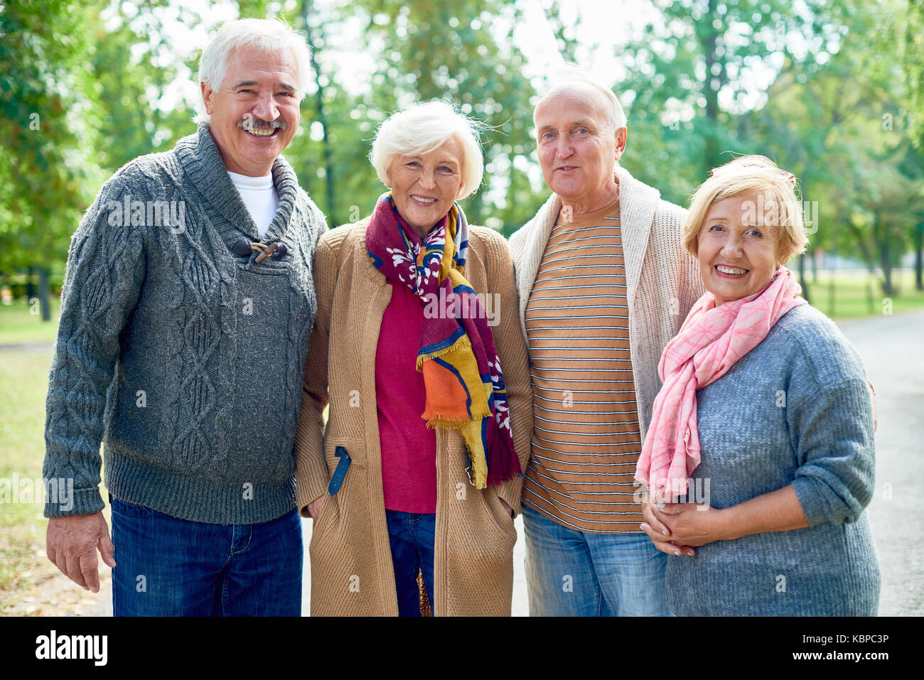 Ritratto di gruppo di allegro senior amici indossando vestiti caldi  guardando la fotocamera con ampi sorrisi pur avendo piacevole passeggiata  al soleggiato parco verde Foto stock - Alamy