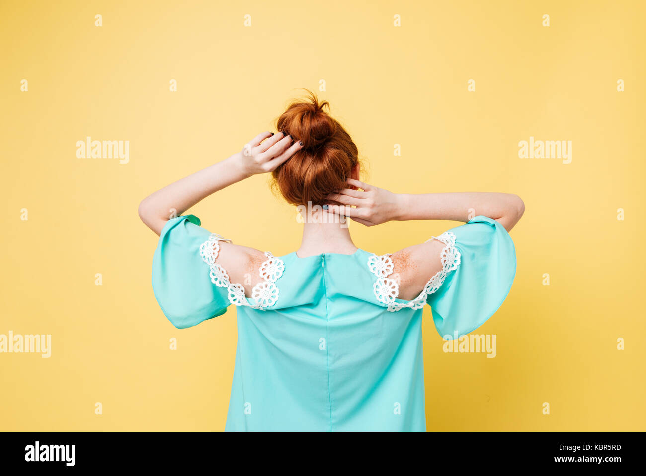 Vista posteriore di zenzero donna nel vestire in posa su sfondo giallo Foto Stock