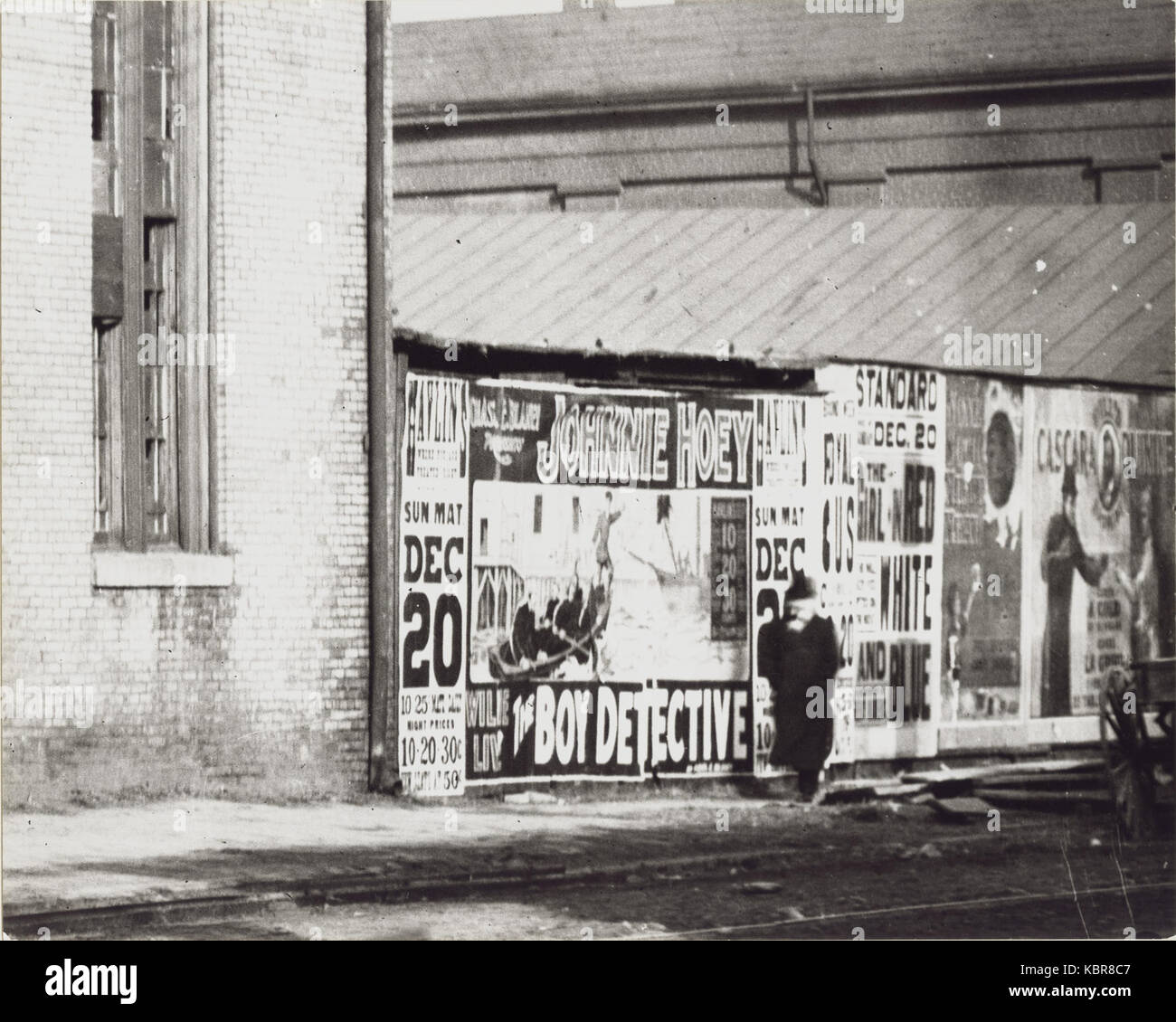Un uomo cammina davanti ad una parete del poster pubblicitari tra cui uno per Johnnie Hoey il ragazzo Detective a giocare a Havlin's Theatre a 600 Walnut Street Foto Stock