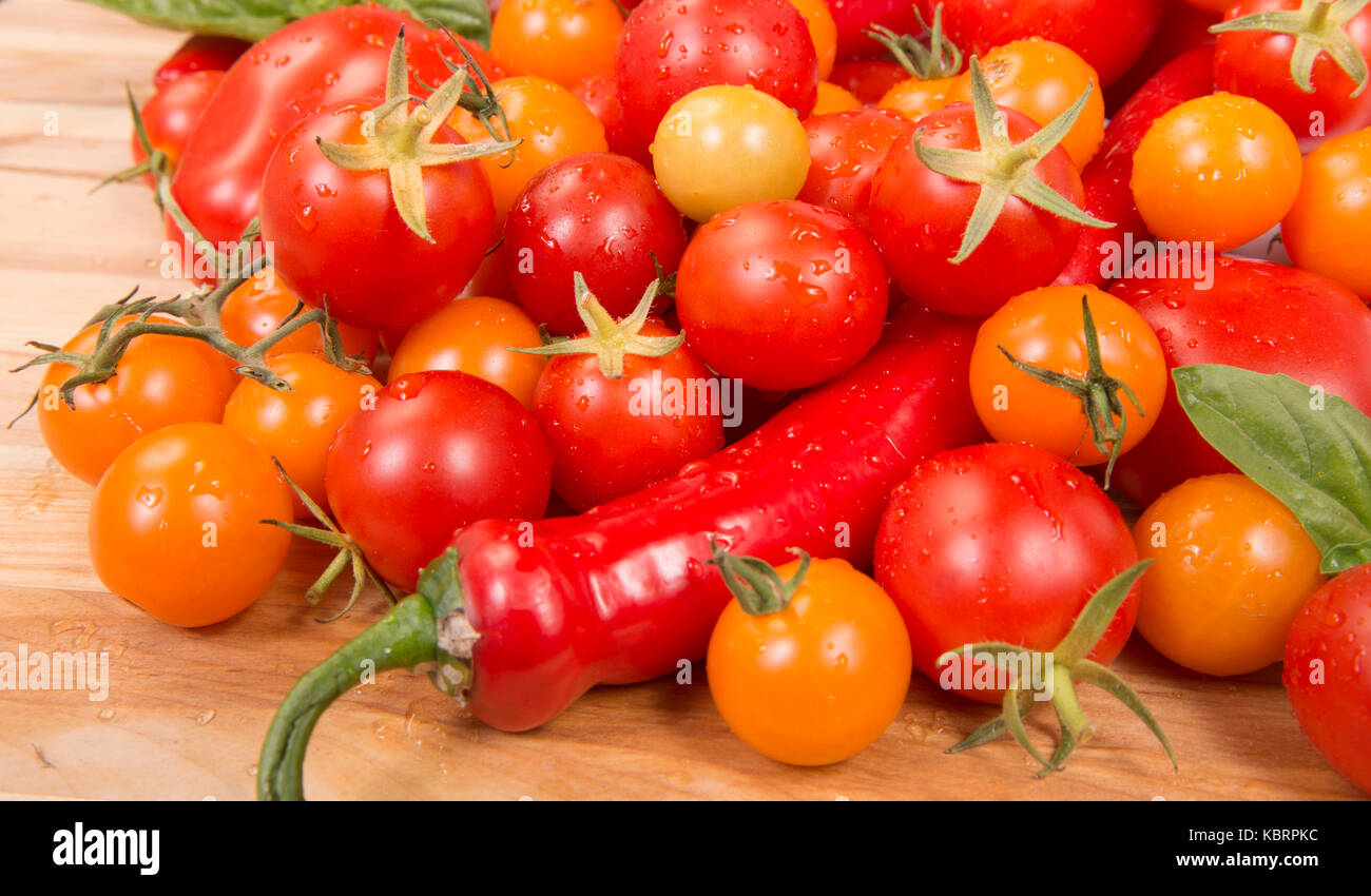 Pomodori freschi, peperoni, con basilico riversandosi su di un tagliere Foto Stock