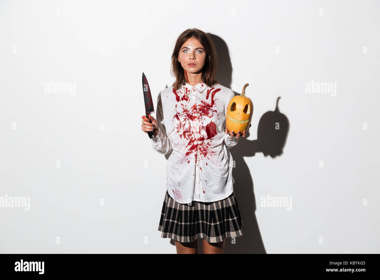 Ammaccati e sanguinosa zombie donna tenere grandi coltelli intagliati e zucca isolate su sfondo bianco Foto Stock