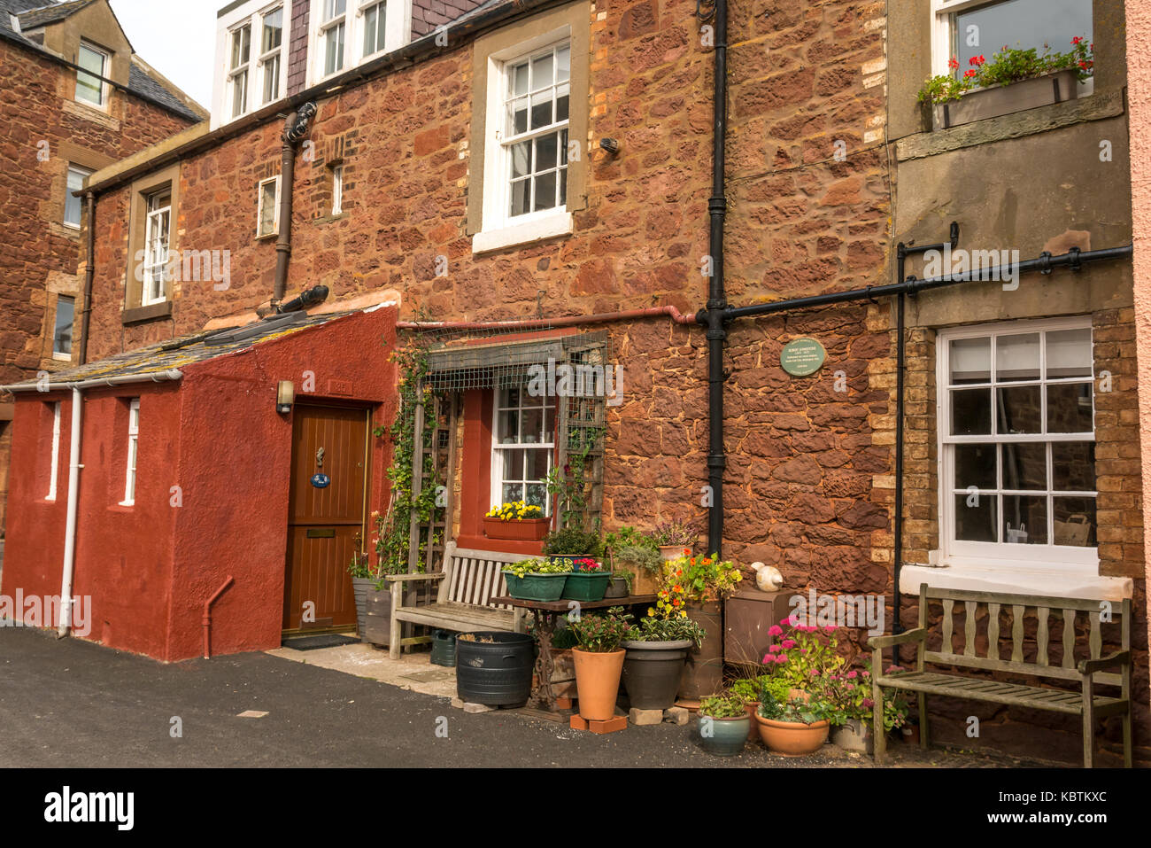 Rosso pittoreschi cottage in pietra arenaria sul lato del porto, North Berwick, East Lothian, Scozia, con vasi di fiori e panchine Foto Stock