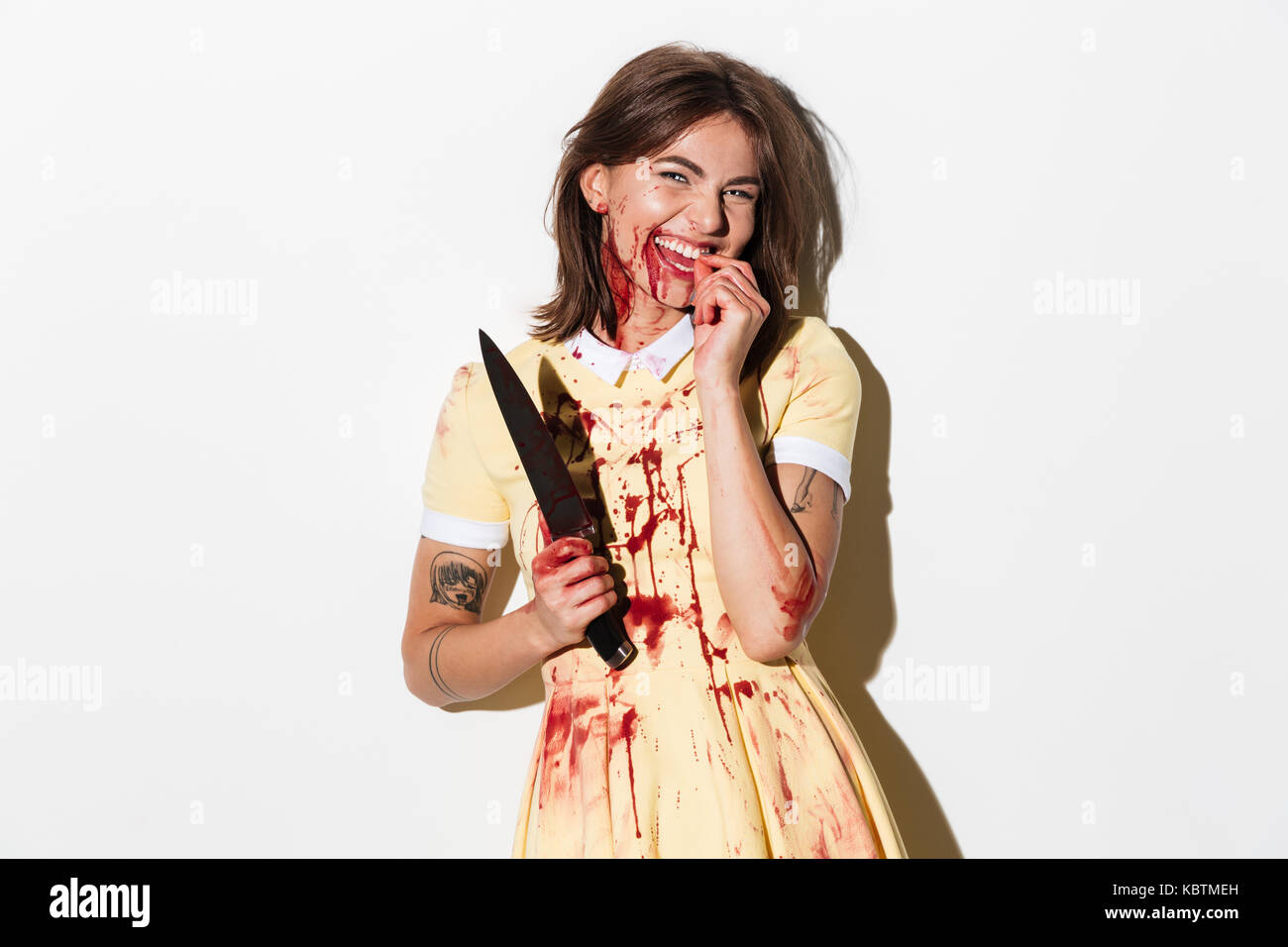 Ammaccati e macchiato di sangue donna zombie in possesso di un coltello e ridere isolate su sfondo bianco Foto Stock