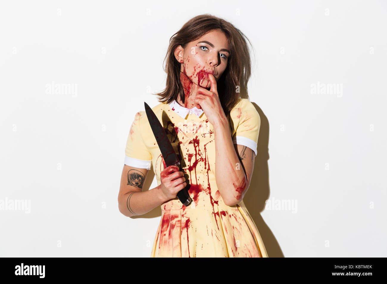 Creepy zombie donna ricoperto di macchie di sangue in possesso di un coltello e guardando la telecamera isolate su sfondo bianco Foto Stock