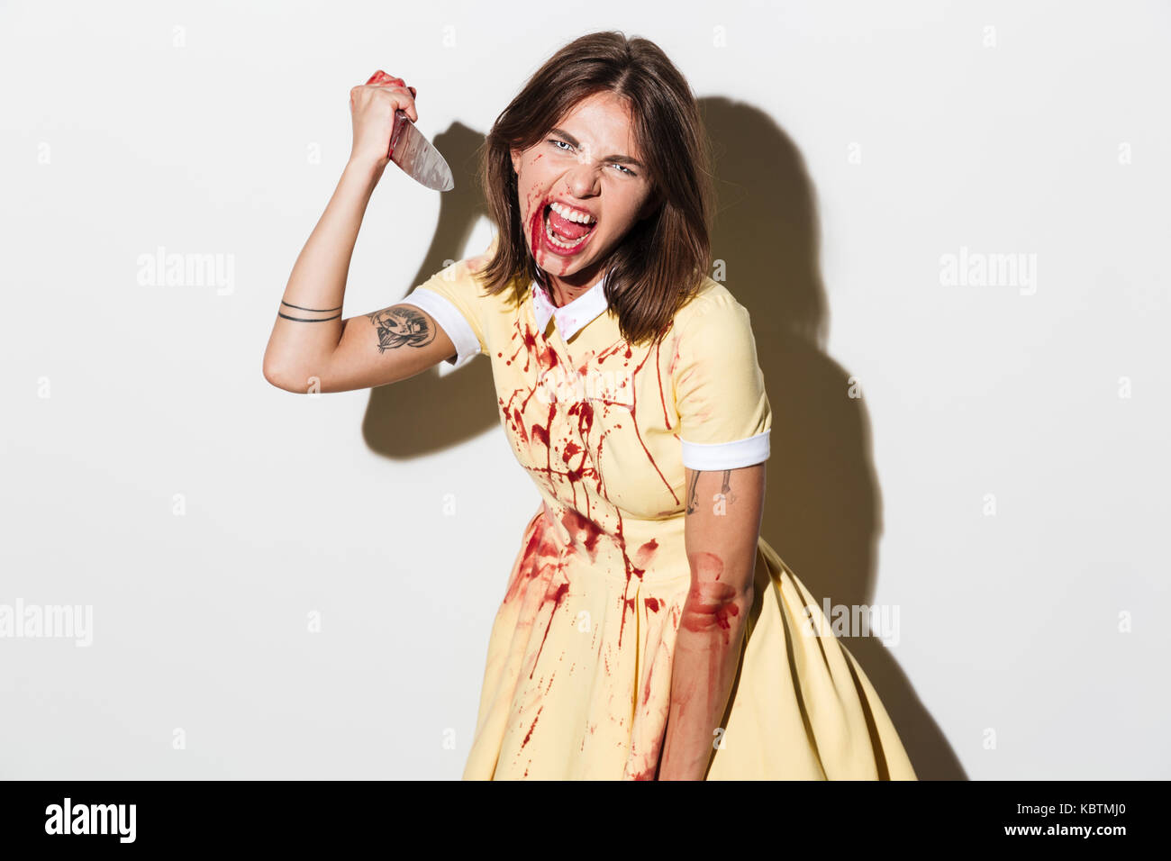 Donna di zombie con ferite e macchie di sangue in possesso di un coltello di grandi dimensioni e pronto ad attaccare isolate su sfondo bianco Foto Stock
