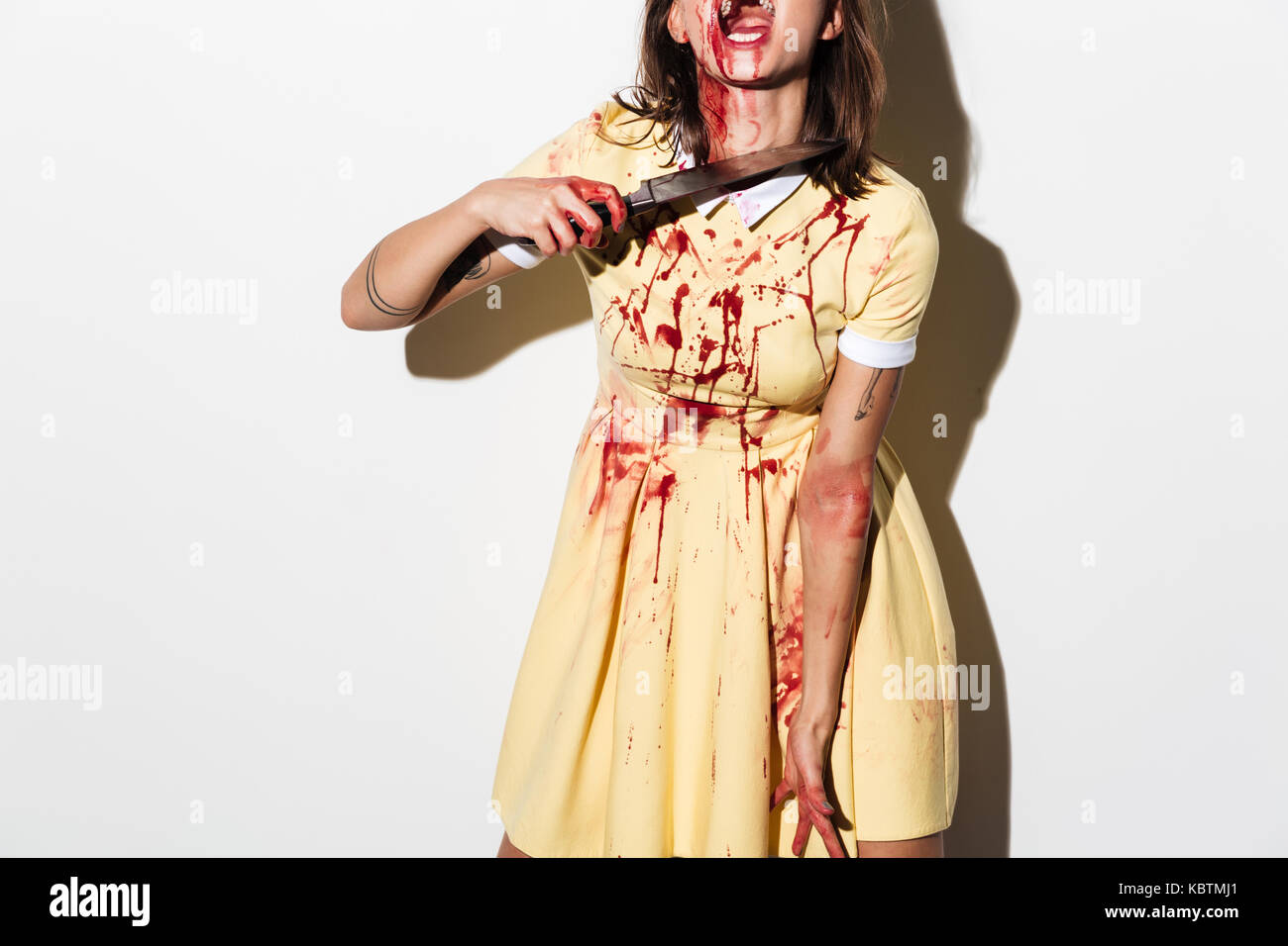 Immagine ritagliata di una donna zombie bleading e feriti in possesso di un coltello a sua gola isolate su sfondo bianco Foto Stock