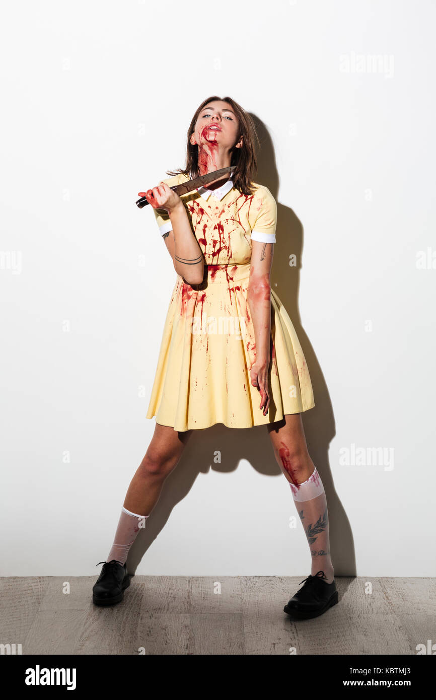 A piena lunghezza Ritratto di mad zombie donna bleading tenendo un coltello a sua gola isolate su sfondo bianco Foto Stock