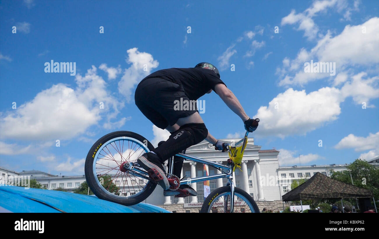 Giovane uomo su bmx bike salti. l uomo facendo torsioni e trucchi su bmx in slow motion cielo blu sullo sfondo Foto Stock