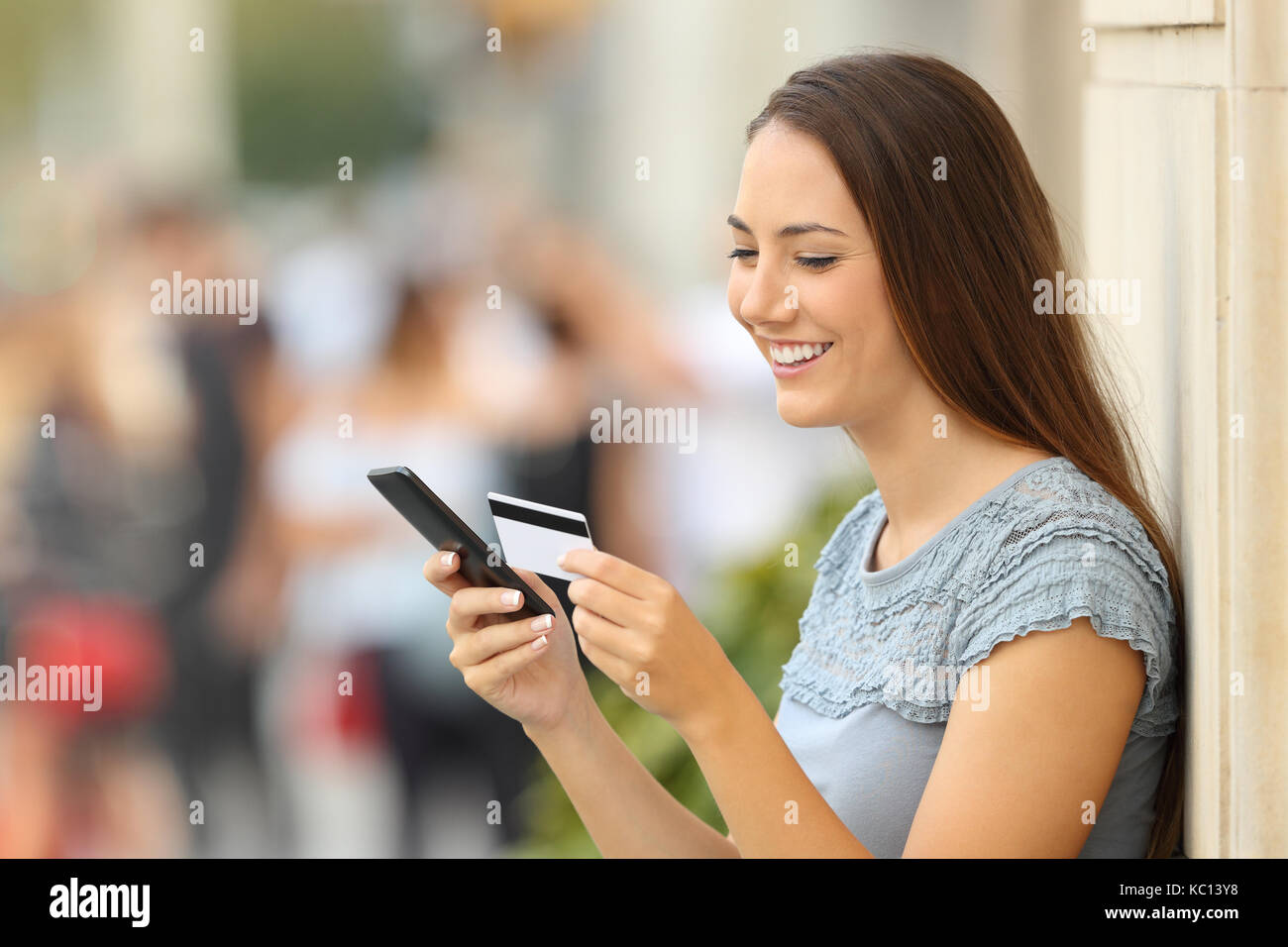Ragazza felice di pagare on line con carta di credito e uno smart phone appoggiato su di una parete sulla strada Foto Stock
