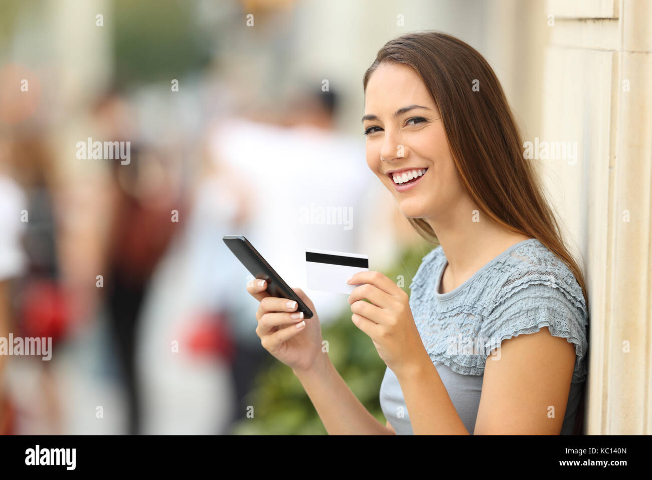 Ritratto di un on line shopper guardando la fotocamera e in possesso di una carta di credito sulla strada Foto Stock