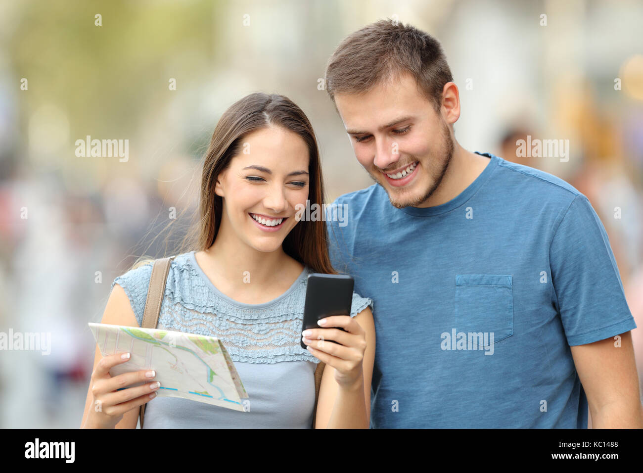 Vista frontale di un paio di felici turisti alla ricerca posizione sulla linea con un telefono e una mappa sulla strada Foto Stock