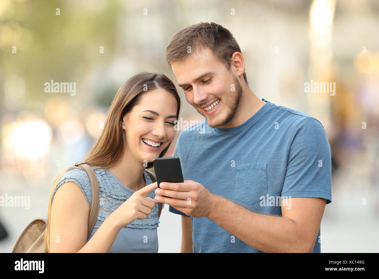 Coppia felice ricerca on line contenuti in uno smart phone in piedi all'aperto sulla strada Foto Stock