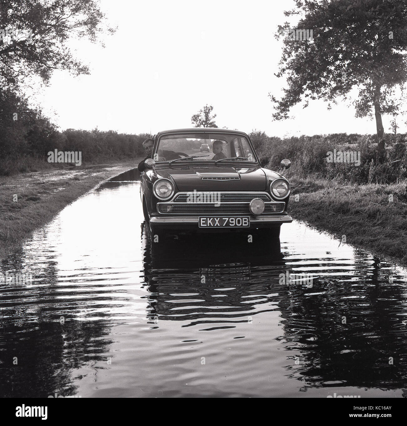 Anni sessanta, storico, padre con bambino in una Ford Cortina Mark 1 auto su un paese allagato lane. Inghilterra, Regno Unito. Foto Stock