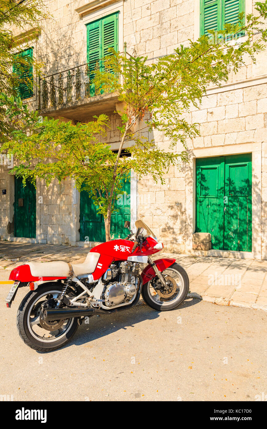 Città Sumartin, Croazia - Sep 13, 2017: rosso moto parcheggio nella parte anteriore di una tipica casa in città sumartin, isola di Brac, Croazia. Foto Stock