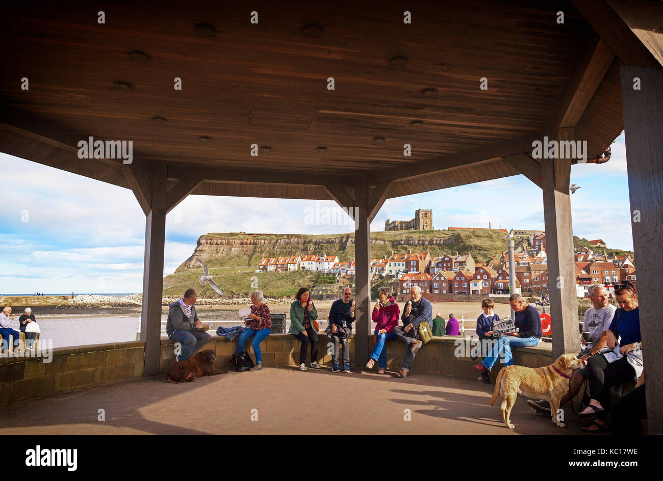Mangiare pesce e patatine e/o di gelato in bandstand a testa di scotch accanto al porto, con Whitby Abbey dietro, North Yorkshire costa, Inghilterra Foto Stock