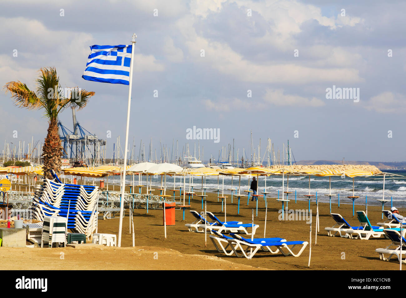 Spiaggia a Larnaca Finikoudas con lettini per prendere il sole.con bandiera greca e marina in background. Foto Stock