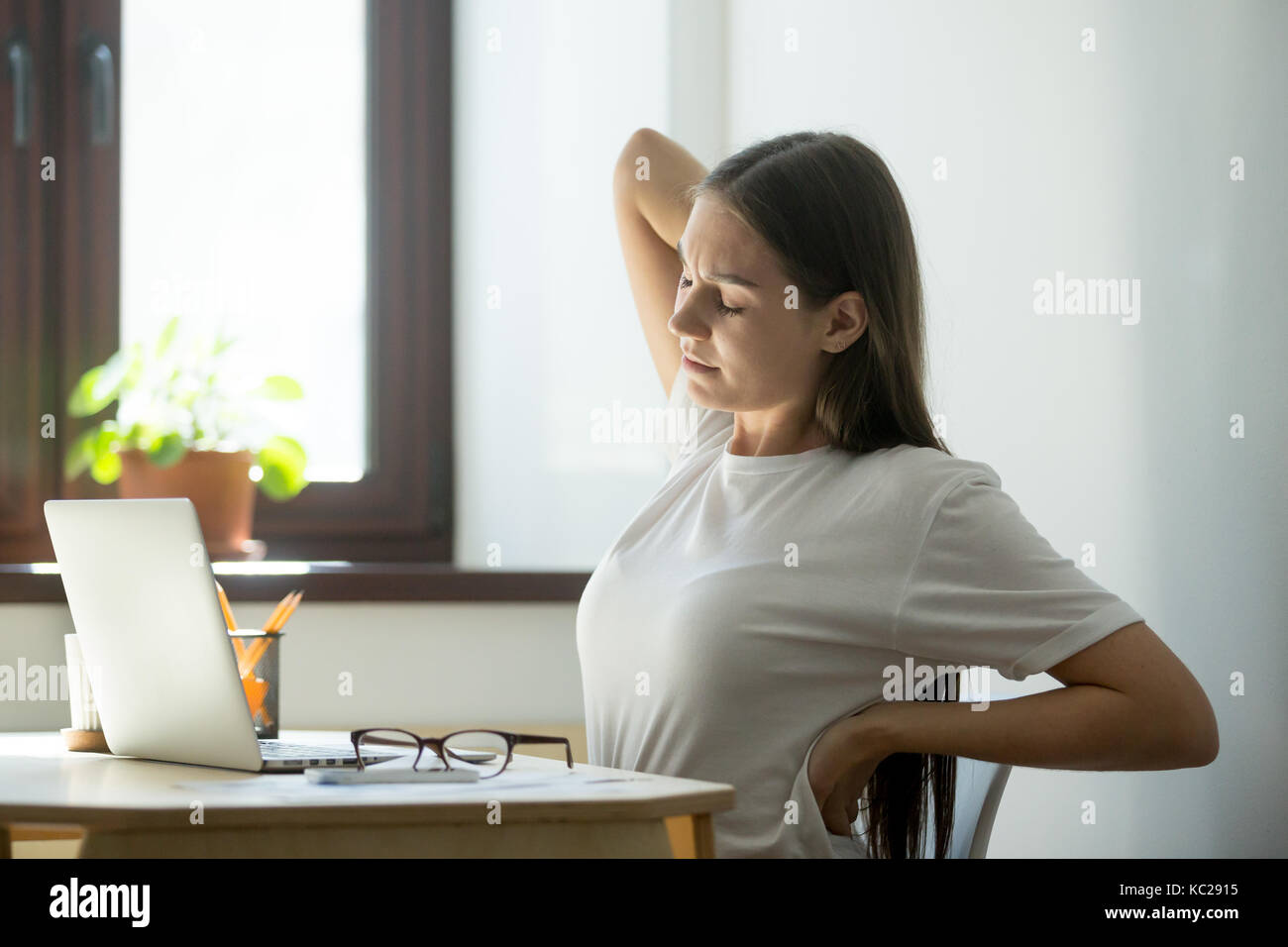 Donna manager tenendo breve pausa dopo una lunga giornata di lavoro sul computer portatile. Ha tolto gli occhiali, chiuse gli occhi e stirando il suo mal di schiena Foto Stock