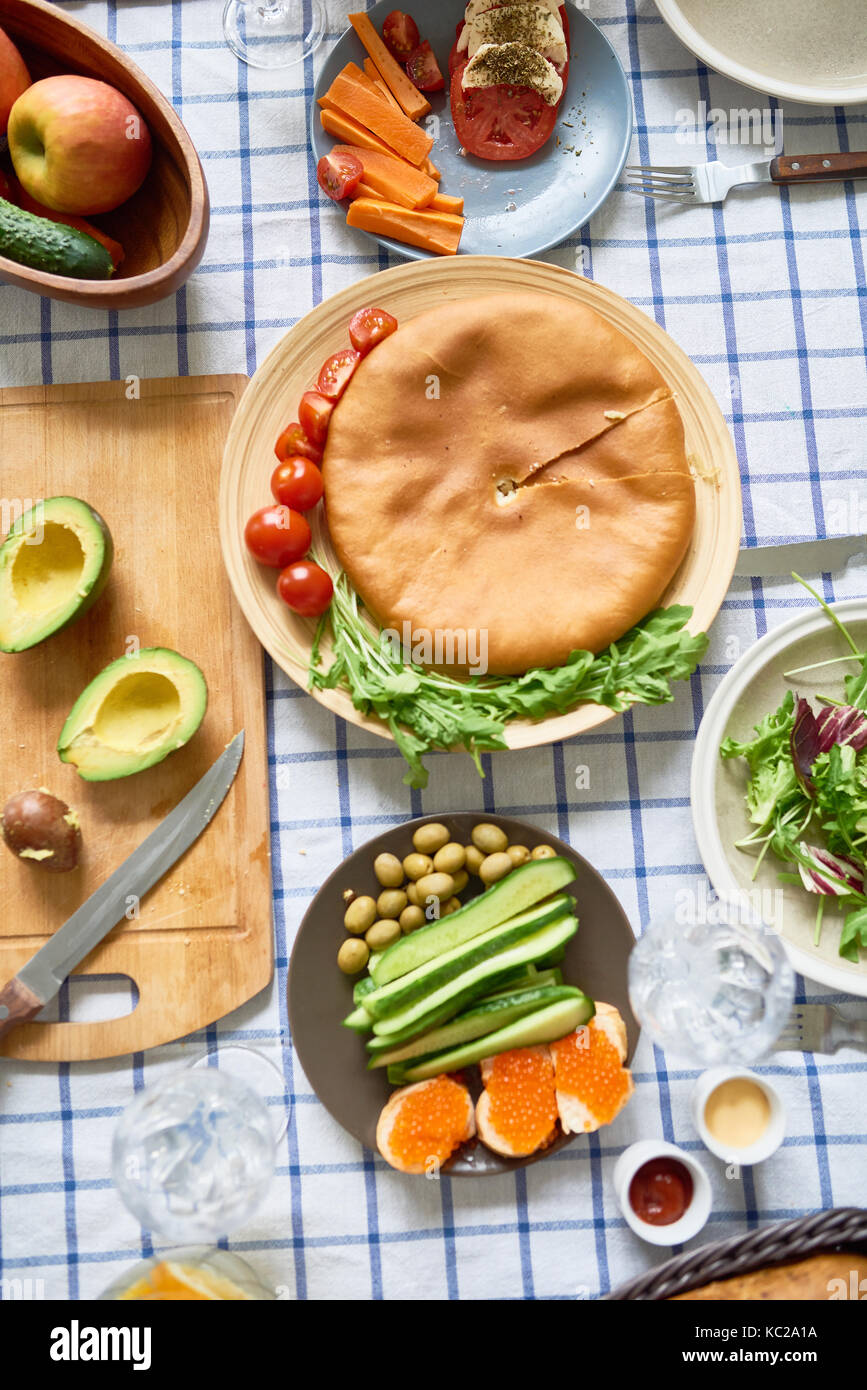 Sopra Visualizza immagine del cibo delizioso sul tavolo sulla tovaglia a scacchi: pane appena sfornato torta circondata da frutti, verdure e insalate Foto Stock