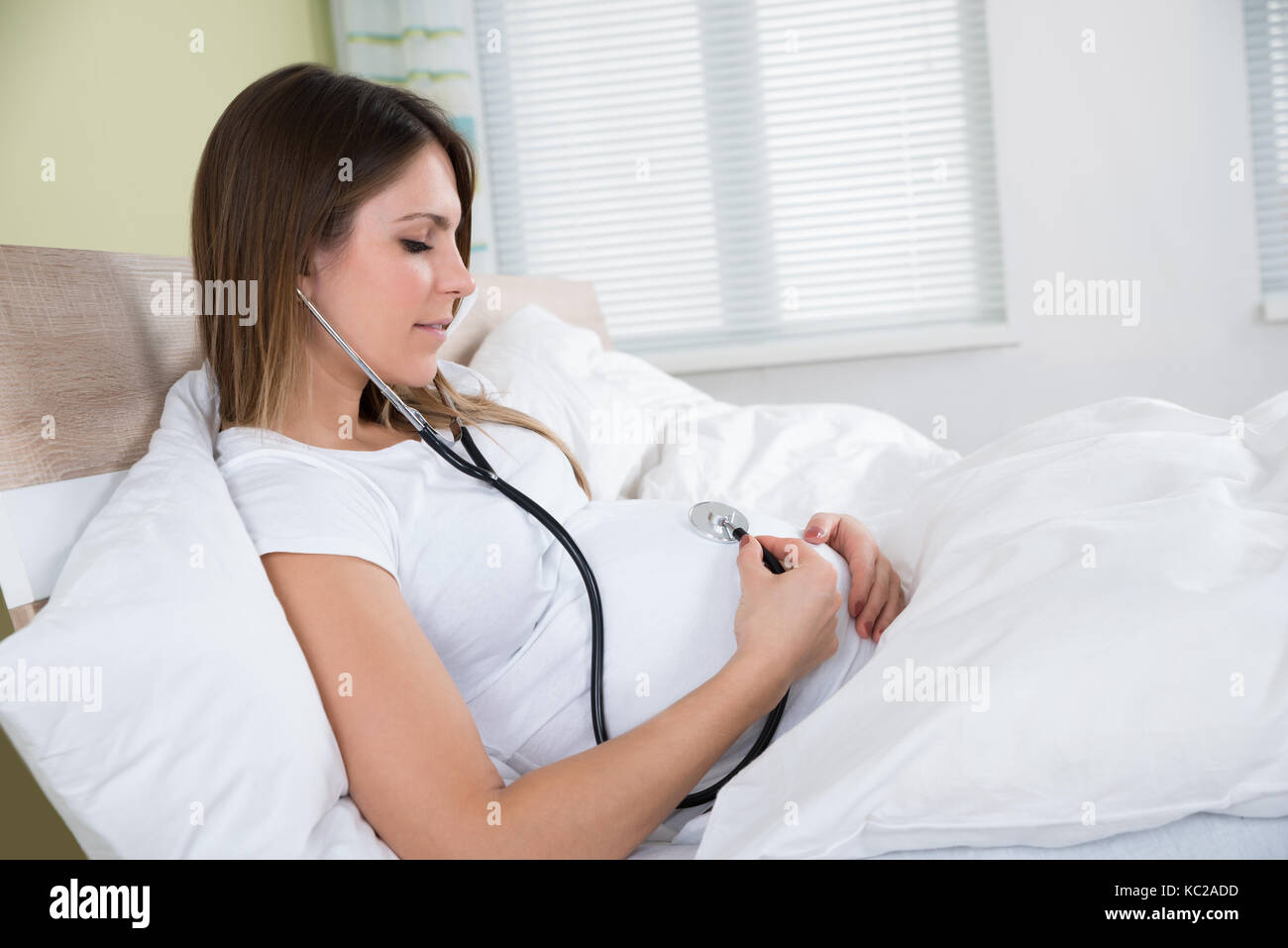 Giovane donna incinta esaminando se stessa con uno stetoscopio Foto Stock