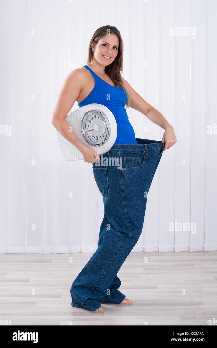 Slim giovane donna con macchina di pesatura che indossa jeans grandi Foto Stock