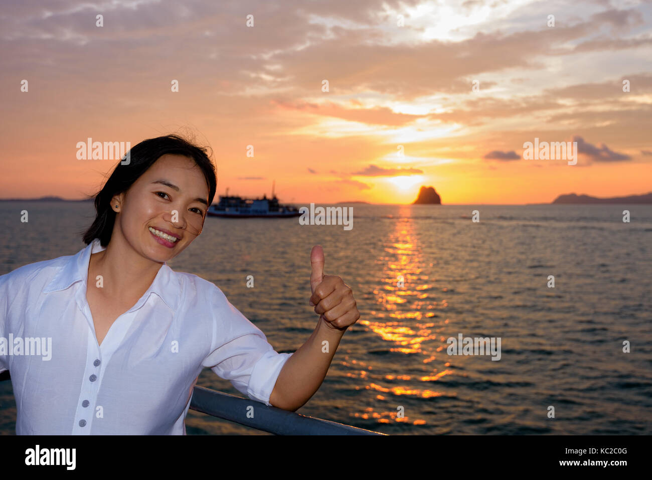 Donne alzare il pollice per ammirare la bellissima natura del cielo colorato e il sole al tramonto sul mare sul ponte di una nave passeggeri durante la crociera t Foto Stock