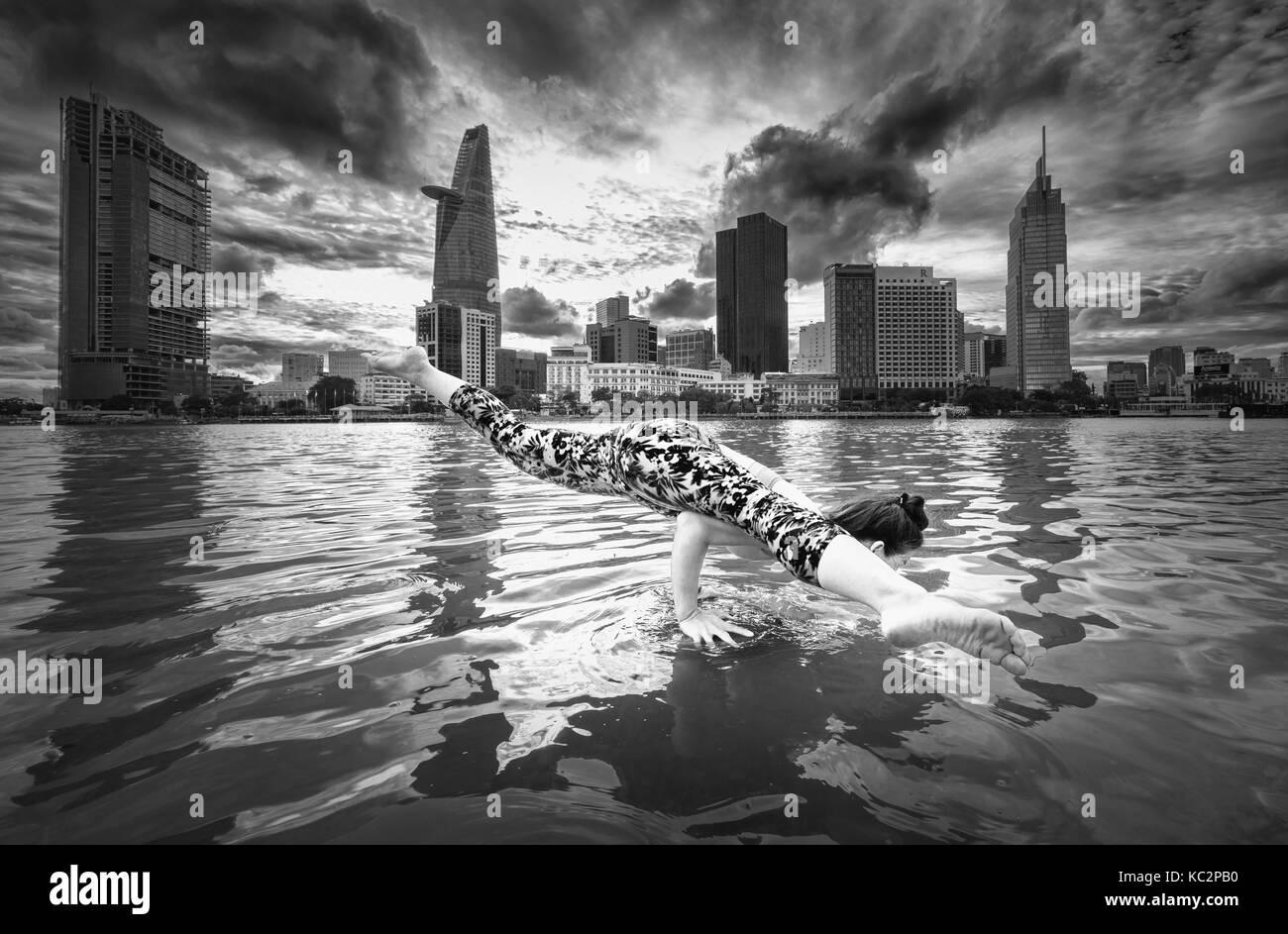 Giovane donna attraente con postura yoga, con reggiseno e pantaloni sportivi, tramonto all'aperto, lungofiume urbano in città Foto Stock