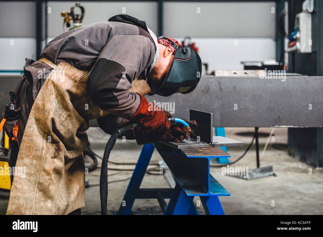 Saldatrice industriale con torcia e casco protettivo nella grande hall di saldatura profili metallici Foto Stock