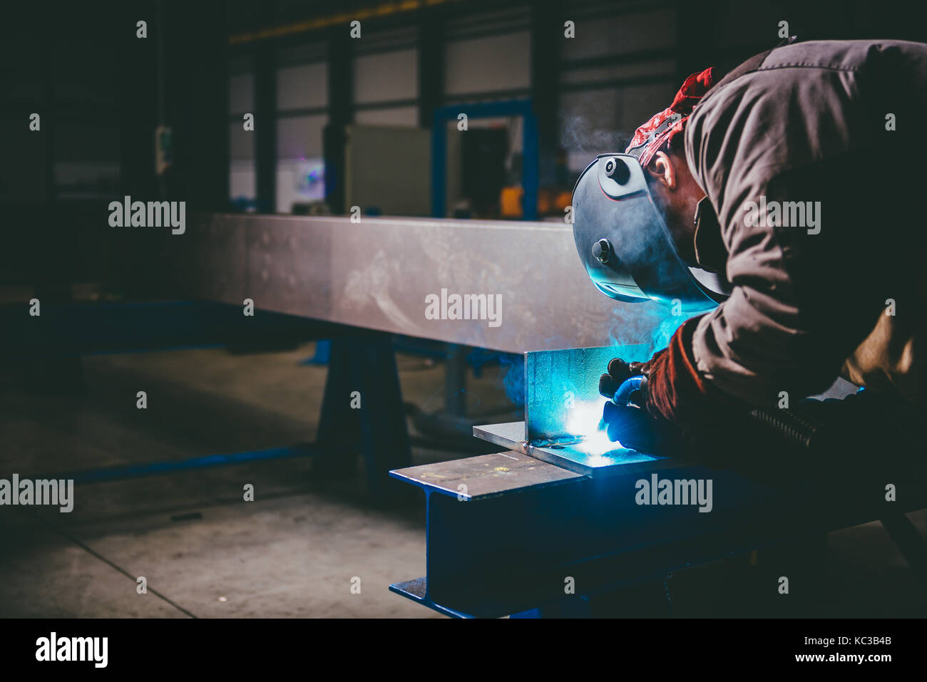 Saldatrice industriale con torcia e casco protettivo nella grande hall di saldatura profili metallici Foto Stock