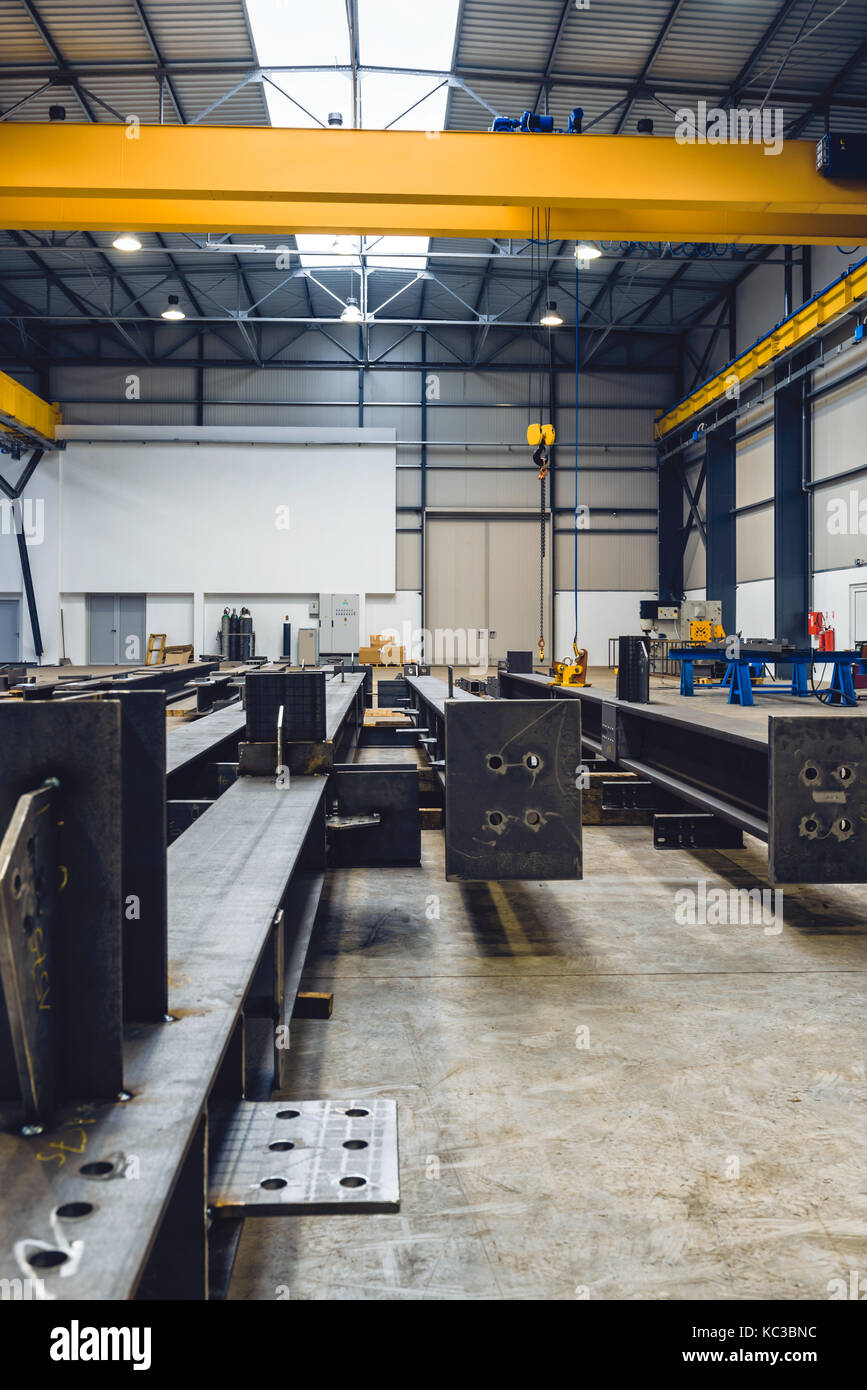 Capannone industriale con taglio, macchine per saldatura e profili metallici con la gru interna in background Foto Stock