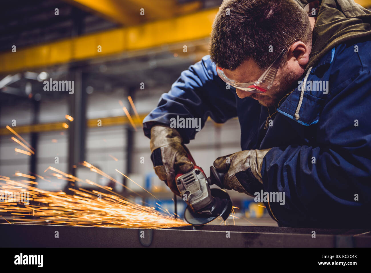 Lavoratore utilizzando smerigliatrice angolare in fabbrica e gettando scintille Foto Stock