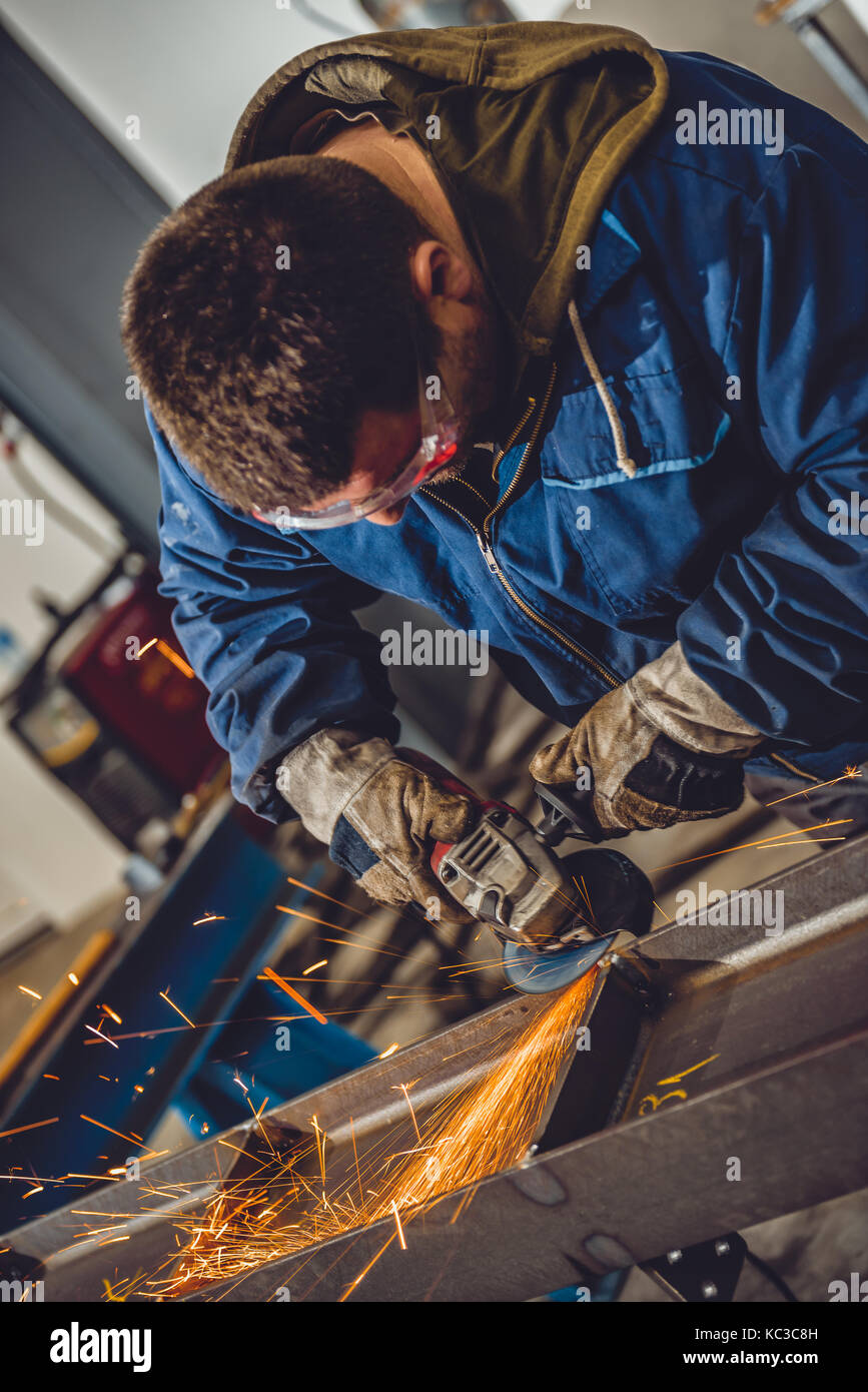 Lavoratore utilizzando smerigliatrice angolare in fabbrica e gettando scintille Foto Stock