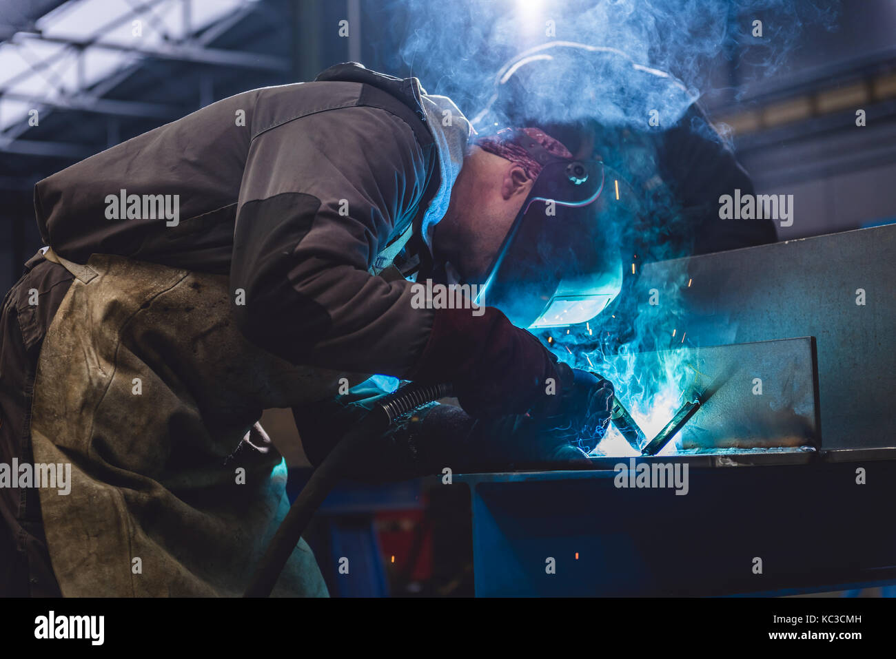 Saldatrice industriale con torcia e casco protettivo nella grande hall di saldatura profili metallici Foto Stock