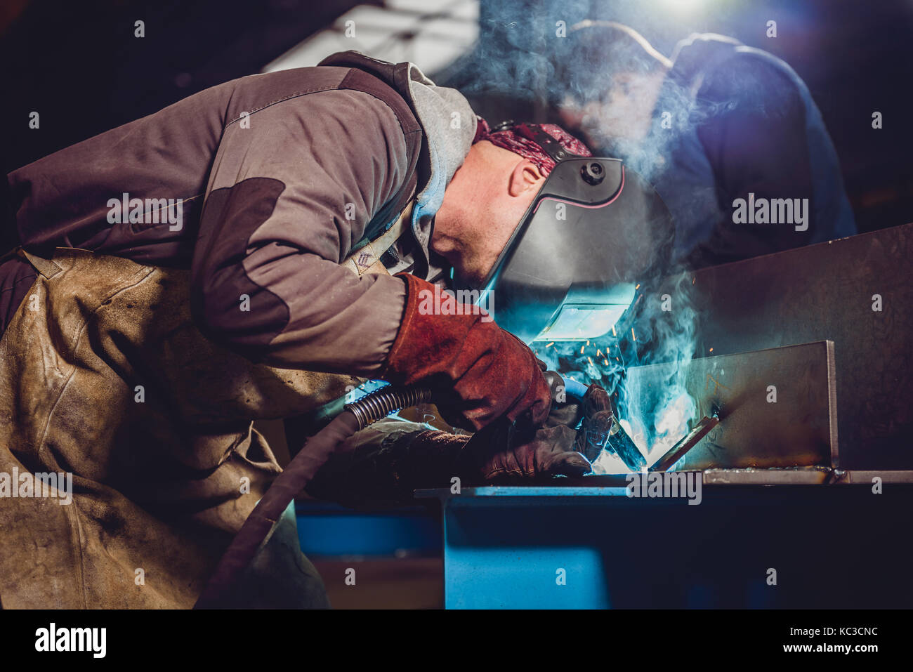 Saldatrice industriale con torcia e casco protettivo nella grande hall di saldatura profili metallici Foto Stock