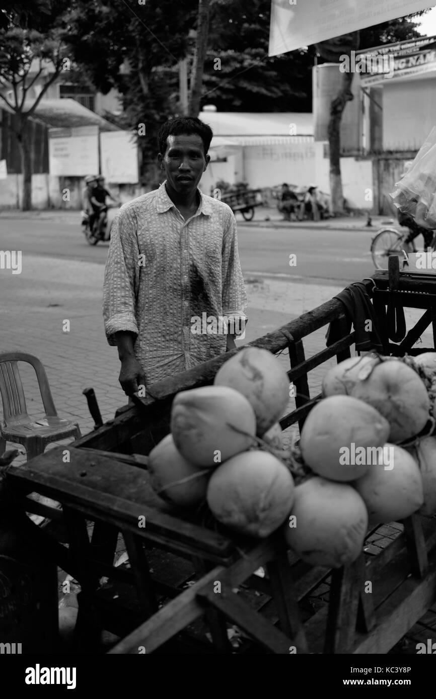 Il sorriso di un uomo vendita di noci di cocco sulla strada, in bianco e nero di tono. Foto Stock