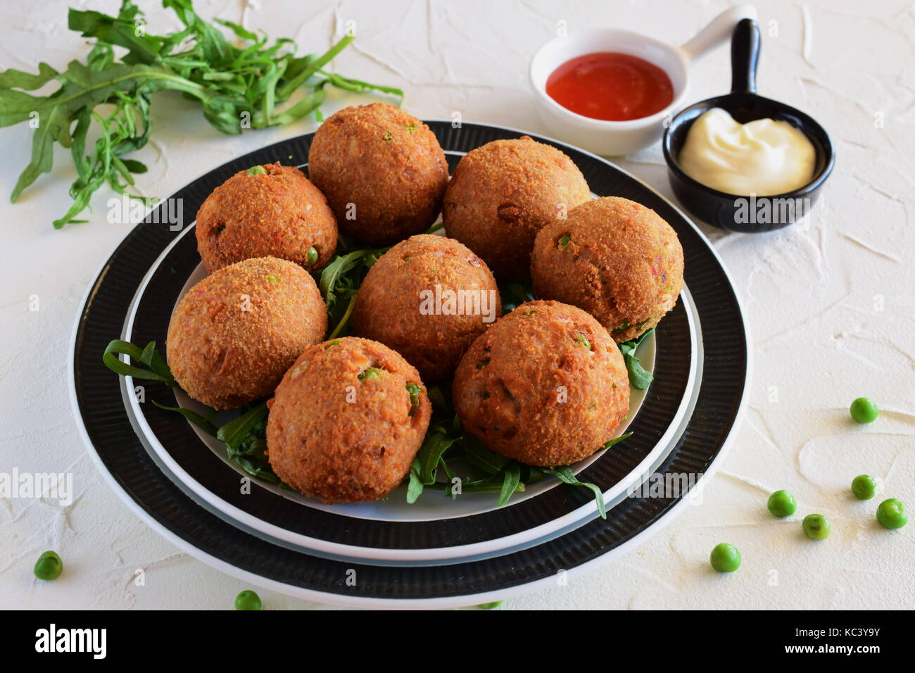 Polpette di pesce con tonno e piselli verdi su una piastra di colore nero su uno sfondo bianco. Il mangiare sano concetto. Foto Stock