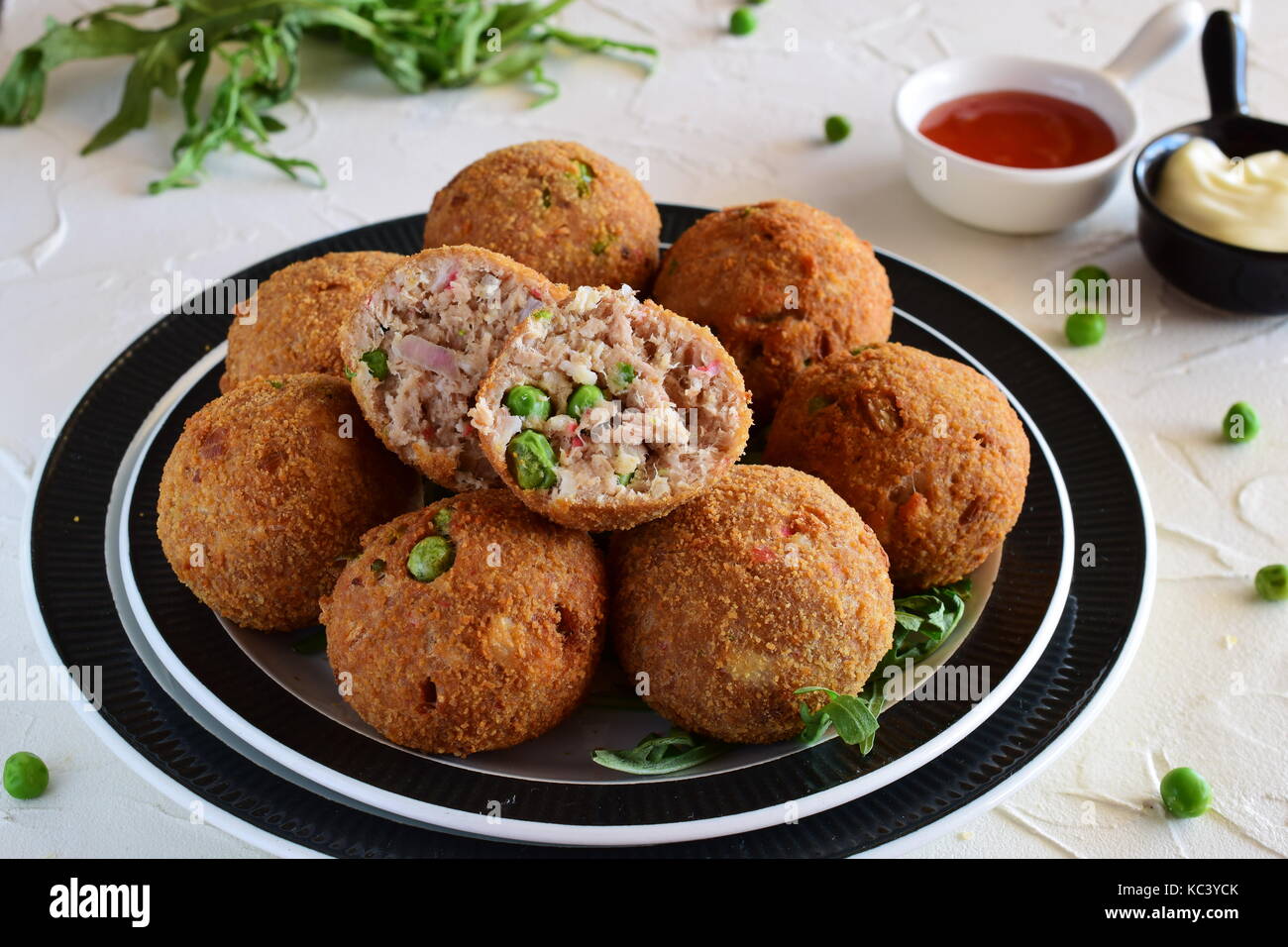 Polpette di pesce con tonno e piselli verdi su una piastra di colore nero su uno sfondo bianco. Il mangiare sano concetto. Foto Stock