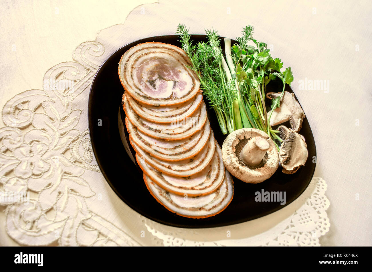 Piatto nero con erbe aromatiche accanto con fette di polpettone di filetto di maiale affumicato Foto Stock