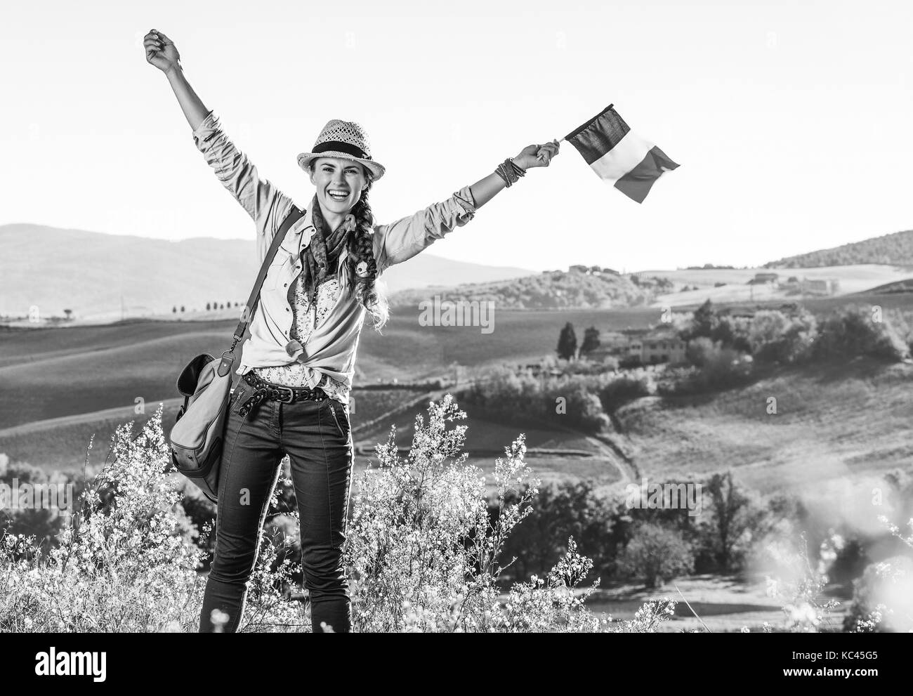 Alla scoperta di magiche vedute della Toscana. sorridente giovane donna escursionista in hat con sacchetto sulla toscana escursione con la bandiera italiana Foto Stock