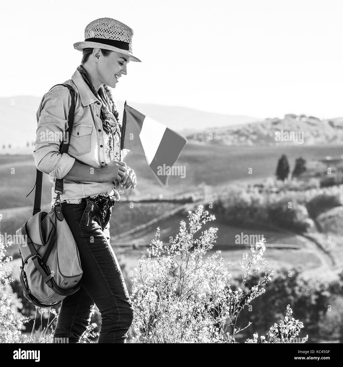 Alla scoperta di magiche vedute della Toscana. sorridente donna avventura escursionista in hat con bandiera italiana gode di vista in toscana Foto Stock