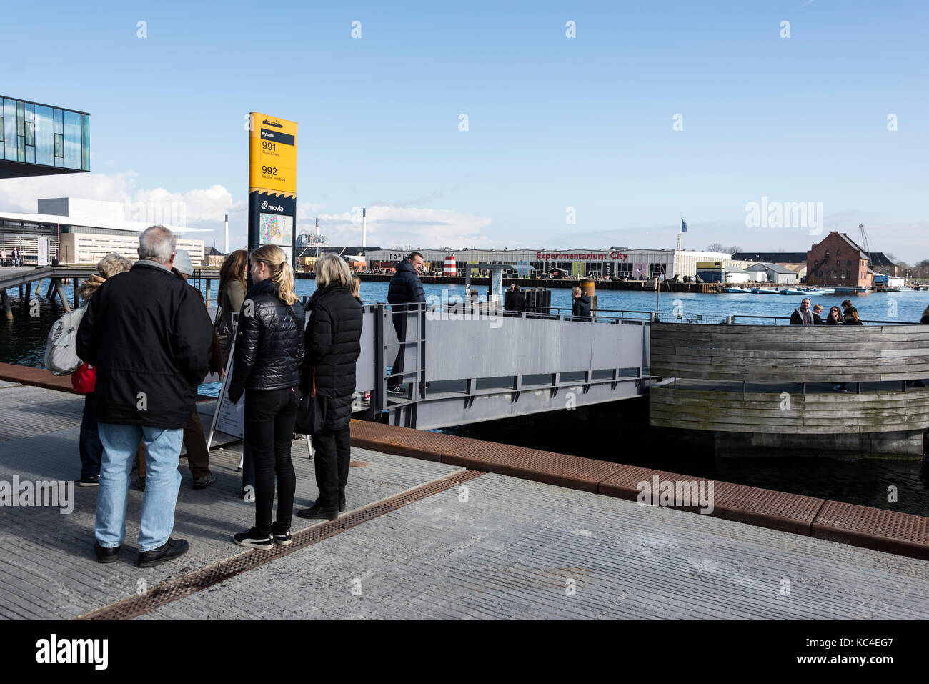 Un gruppo di turisti in attesa dell'arrivo del bus giallo del porto di Copenaghen (Københavns Havnebusser) che serve la lunghezza del Copenhag Foto Stock