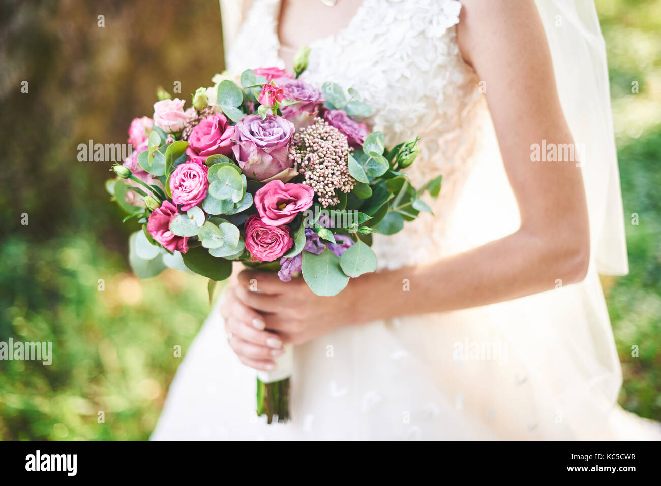 Sposa in un abito bianco tenendo un mazzo di fiori viola e verde su uno  sfondo di erba verde Foto stock - Alamy